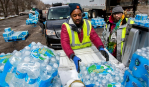 Two men wearing vests are engaged in the process of loading water bottles onto a truck for delivery.